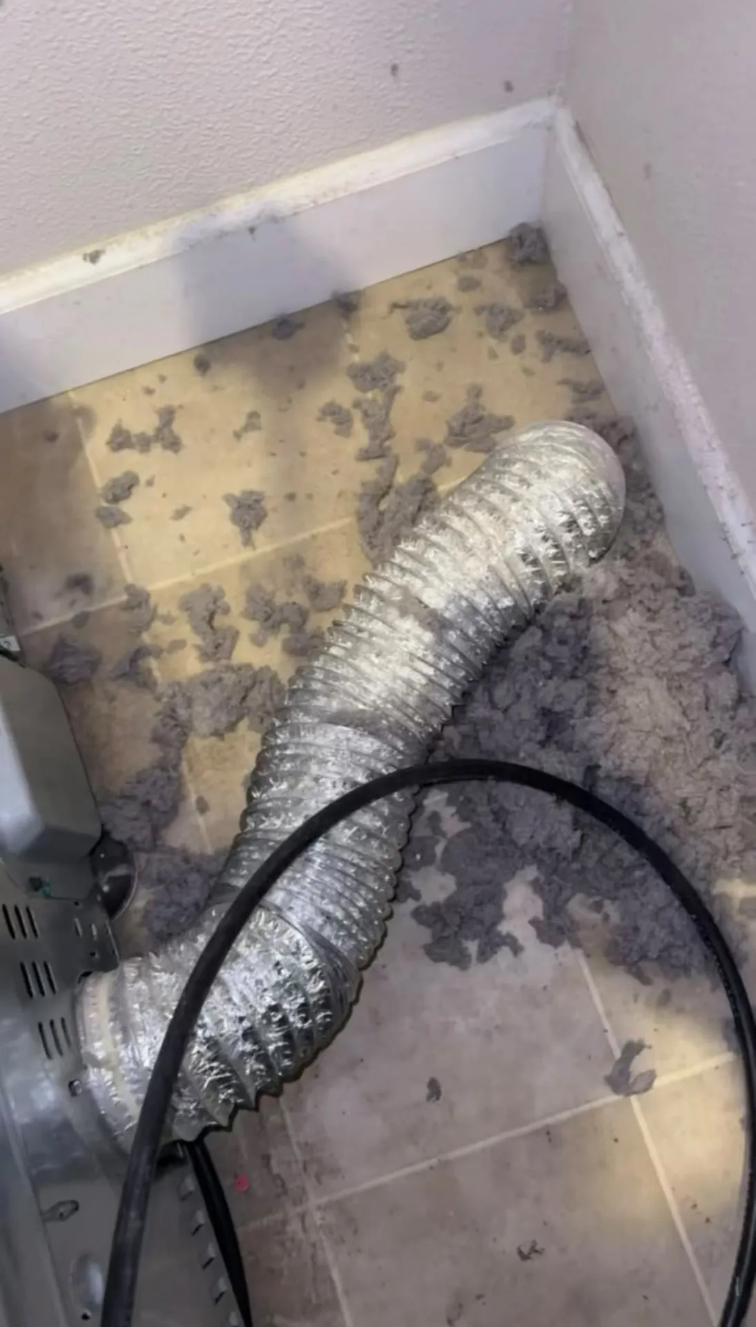 Foil dryer vent hose on a tile floor surrounded by removed lint