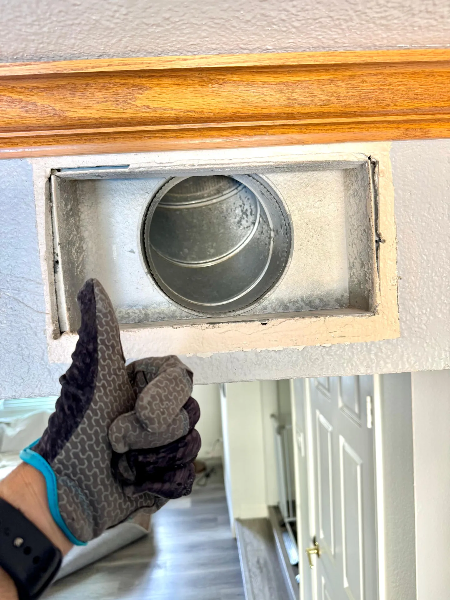 Gloved thumbs-up beside an uncovered metal wall duct opening